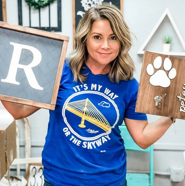 Artist wearing It's My Way or the Skyway t-shirt holding pieces of her art