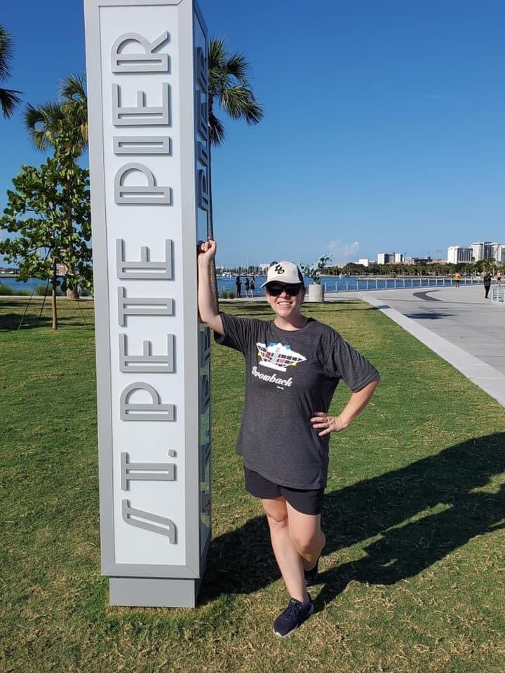 Woman standing next to St. Pete Pier sign wearing a Wide Sky designed Throwback St. Pete Pier t-shirt